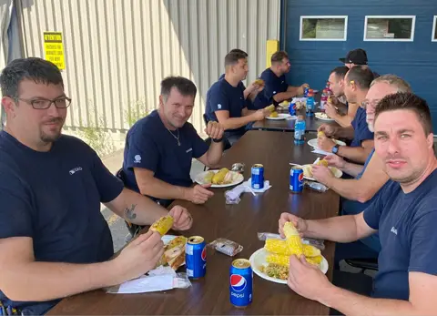 Des employés d’usine de Garaga St-Georges savourant du bon blé d’Inde au cours du dîner annuel du retour des vacances.
